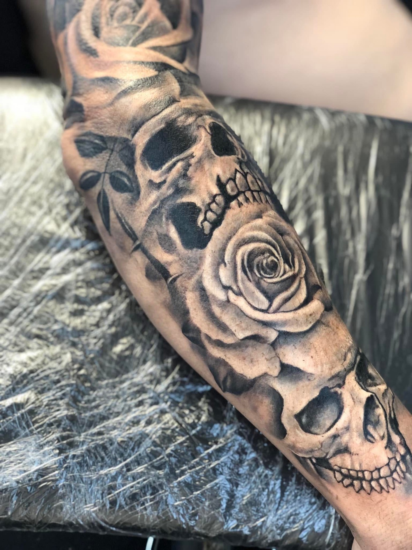 Koponyák és rózsa realisztikus sleeve tetoválás alkaron
